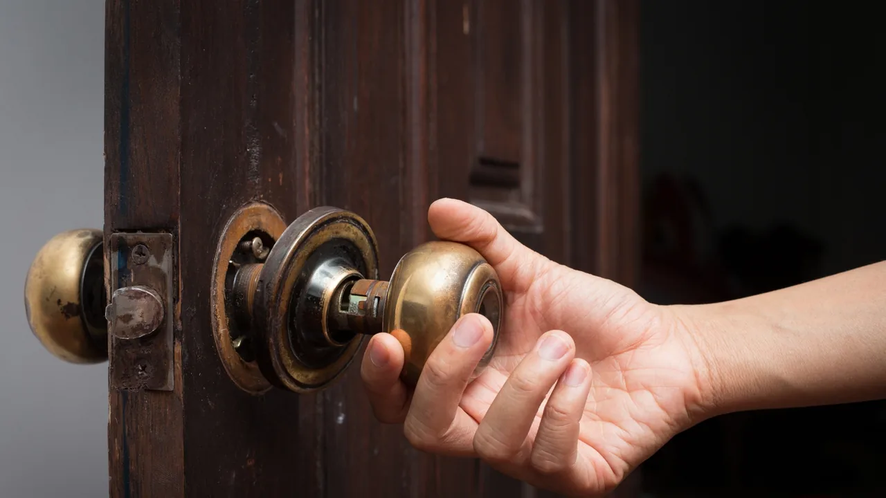 A hand turning a worn brass doorknob on an old door