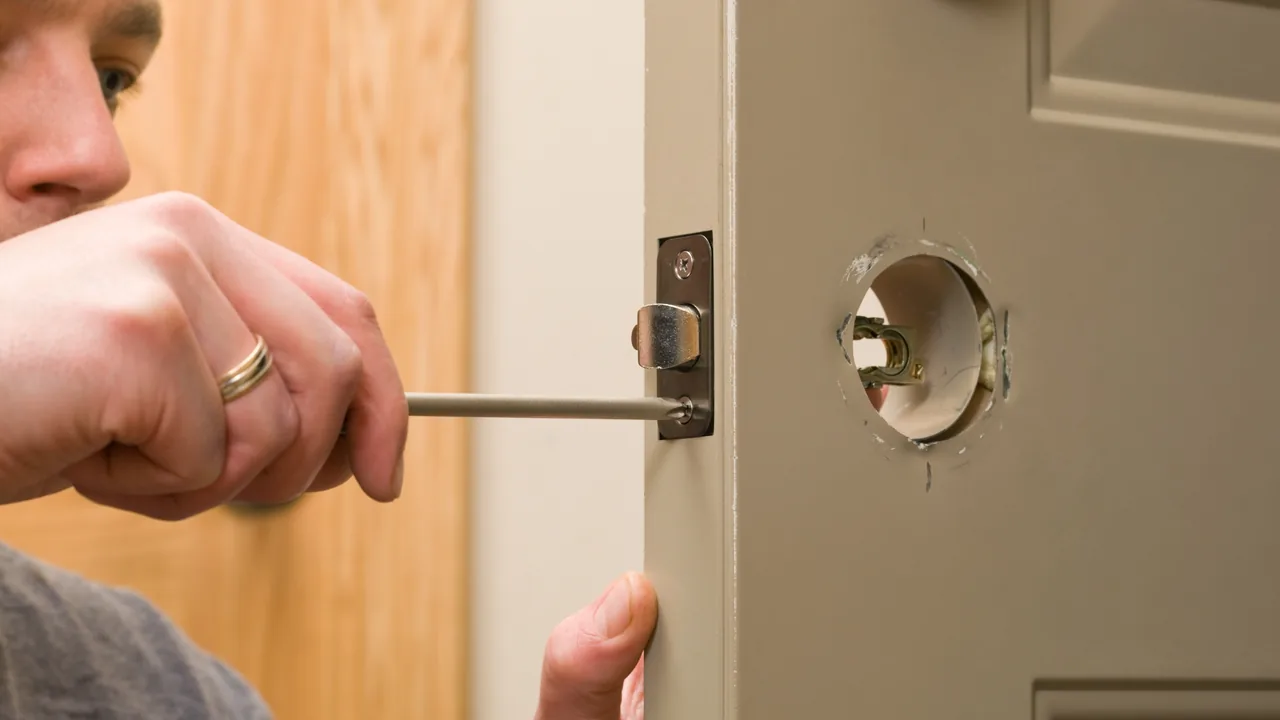 A locksmith adjusting a door latch and strike plate so the door closes properly